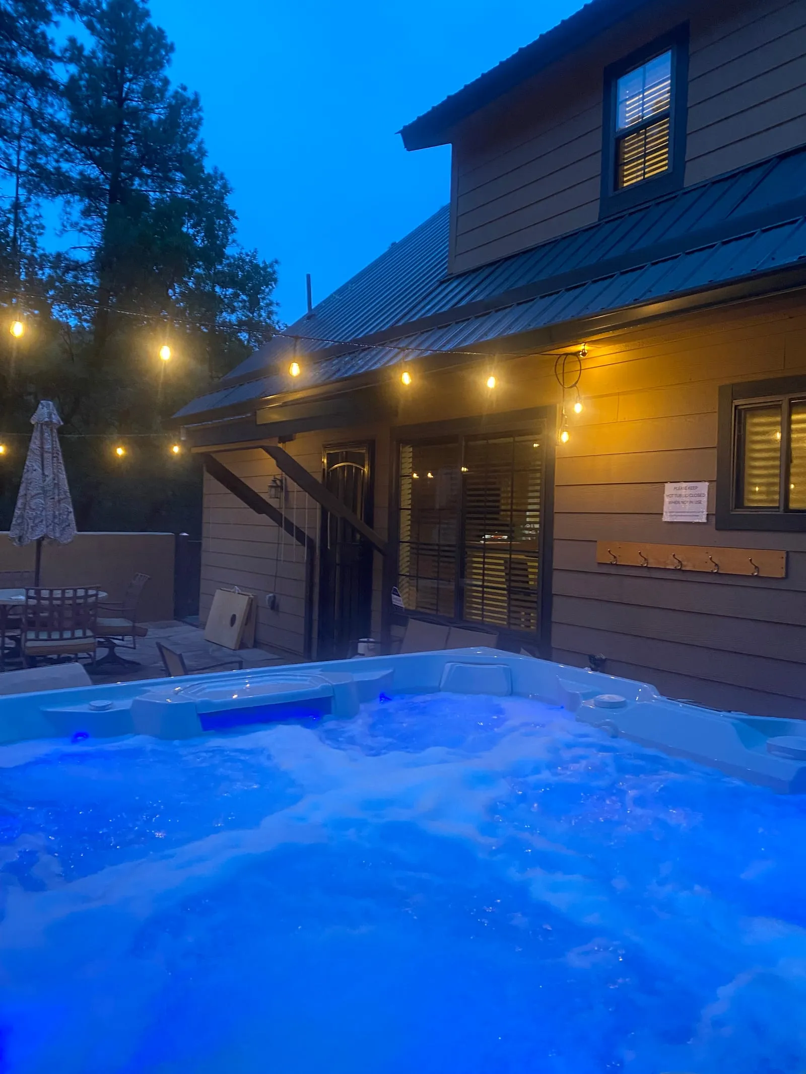 The A-frame cabin glowing at dusk, the private hot tub lit on the deck