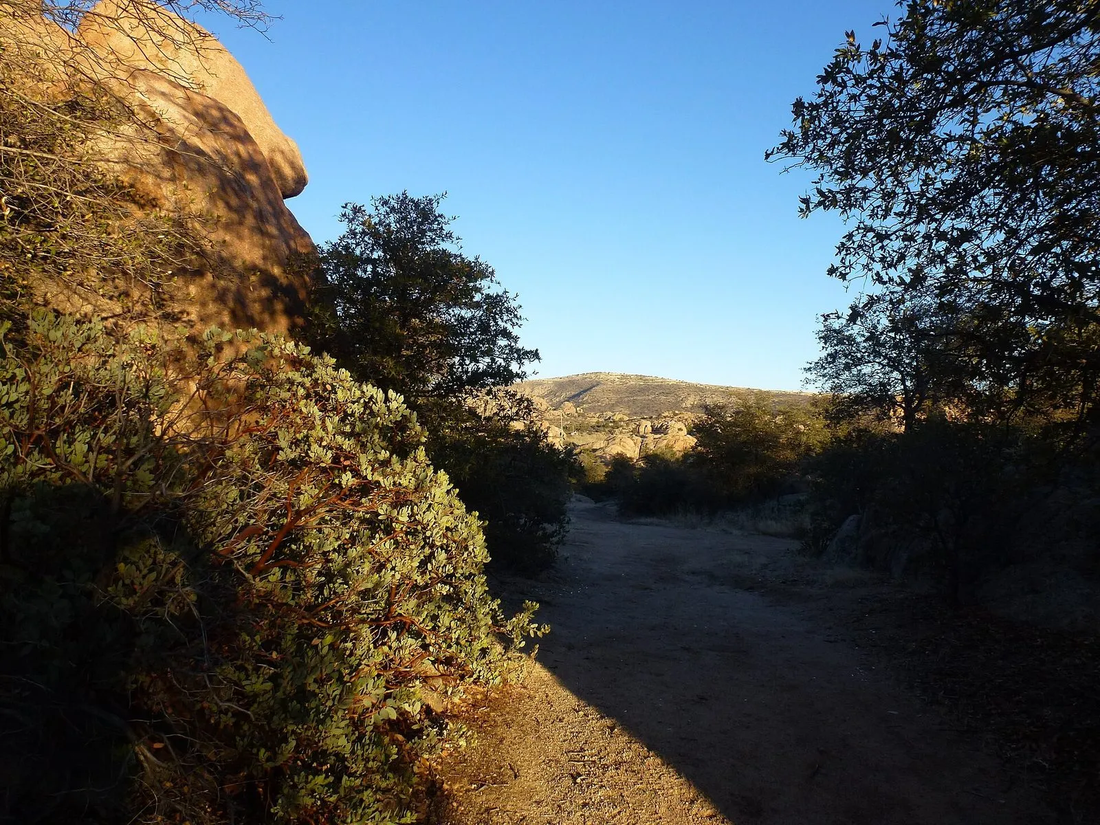 A path running between rounded granite boulders under a deep blue sky in the Granite Dells at Prescott